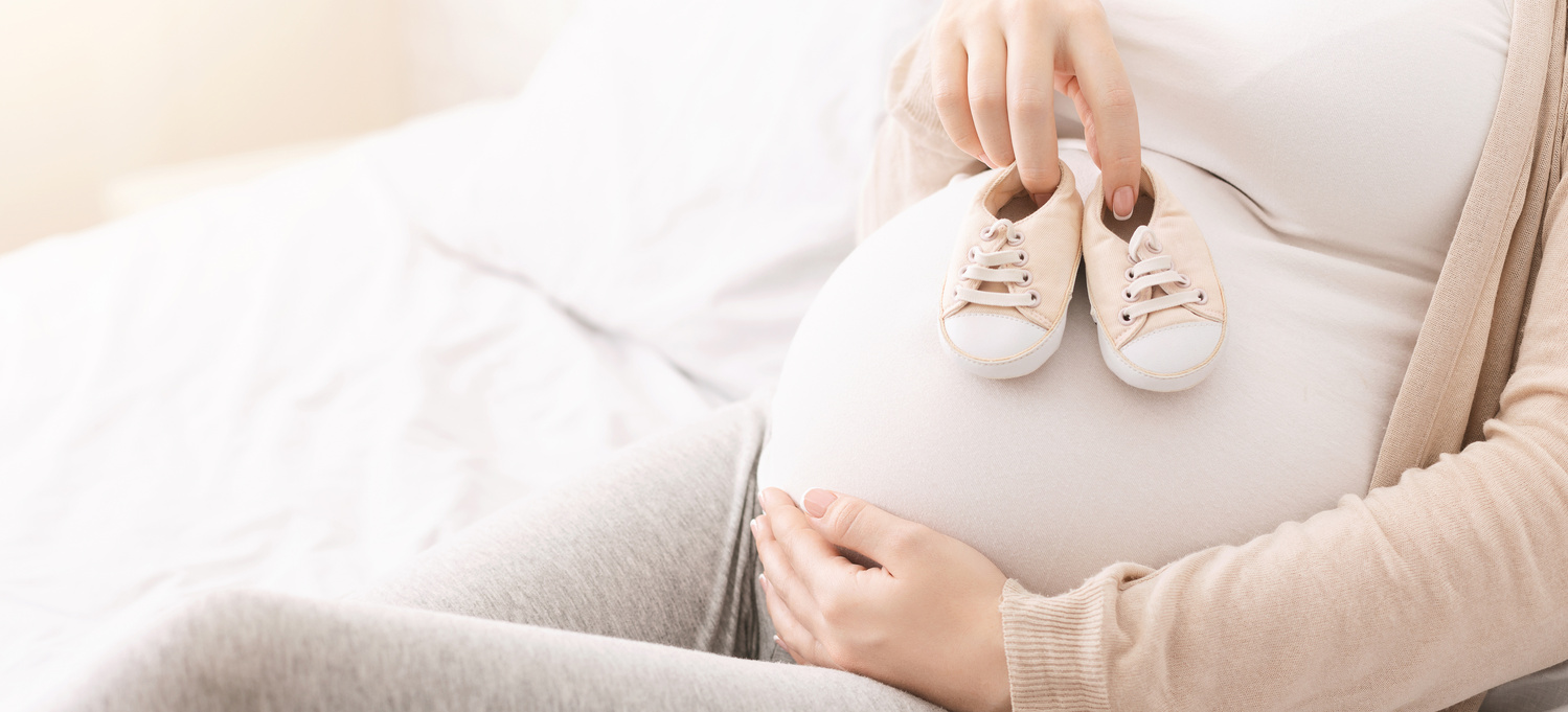 Schwangere Frau hält Babyschuhe auf ihrem Bauch