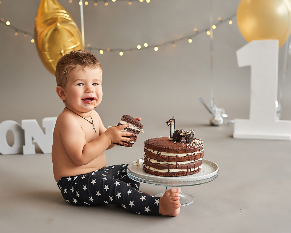 Ein einjähriger Junge hält ein Stück Schokoladenkuchen in den Händen, um seinen Geburtstag zu feiern