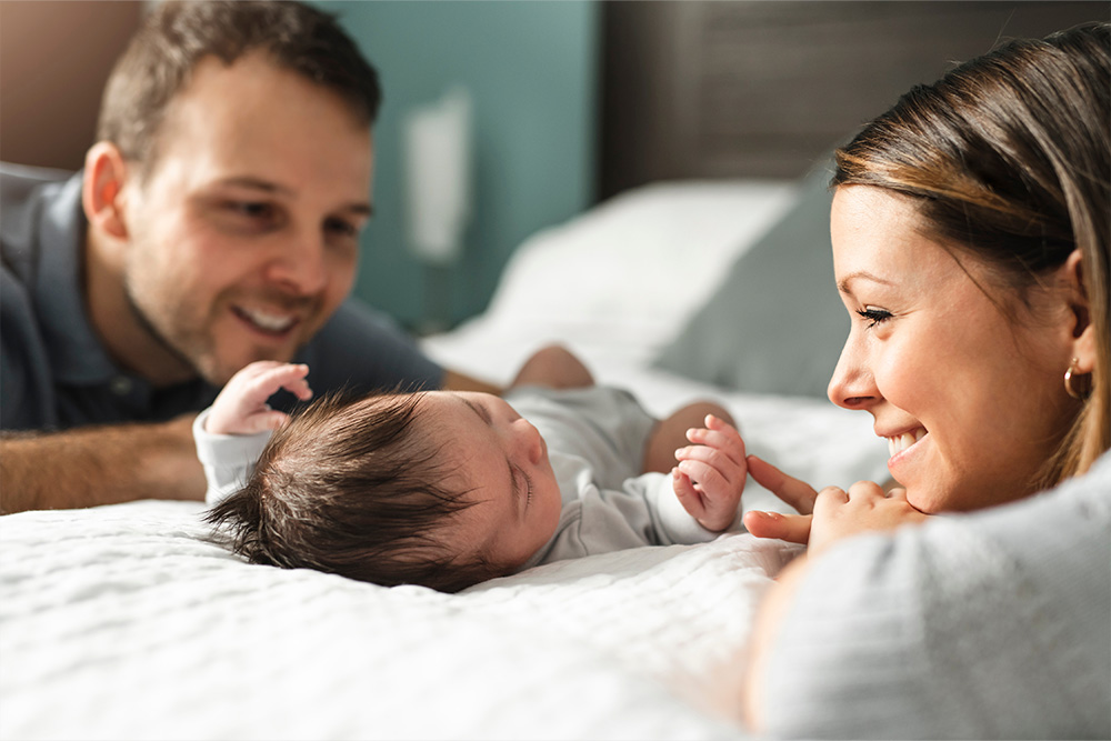 Die Eltern betrachten das schlafende Neugeborene auf dem Bett liegend