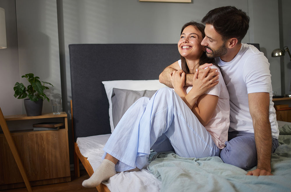 Ein Paar, das im Bett lacht und sich umarmt, und einen gemütlichen, glücklichen Moment zusammen teilt.