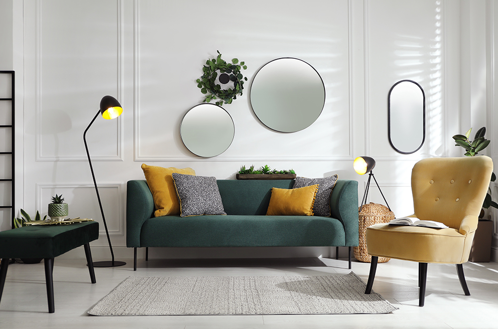 Modernes Wohnzimmer in hellen Farben mit grünem Sofa, gelben Kissen und runden Spiegeln an der Wand.