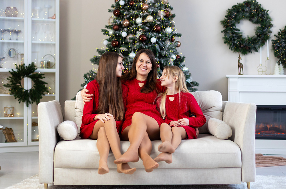 Mutter und ihre Töchter in roten Kleidern verbringen gemeinsam die Weihnachtszeit am Tannenbaum.