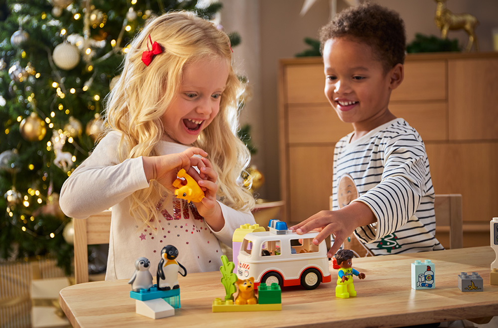 Zwei Kinder spielen mit LEGO-Steinen unter dem Weihnachtsbaum.