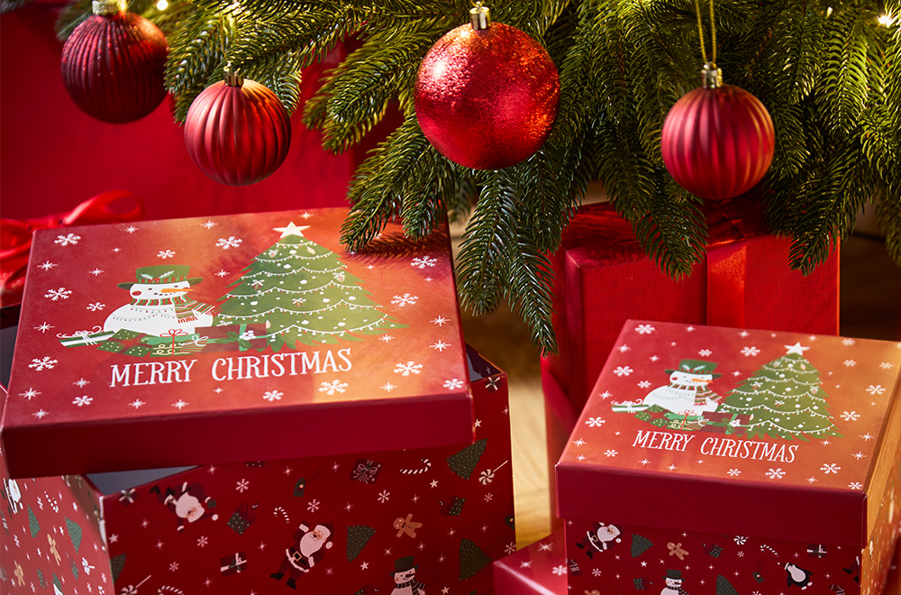 Geschenkboxen mit Weihnachtsmotiven neben dem Weihnachtsbaum.