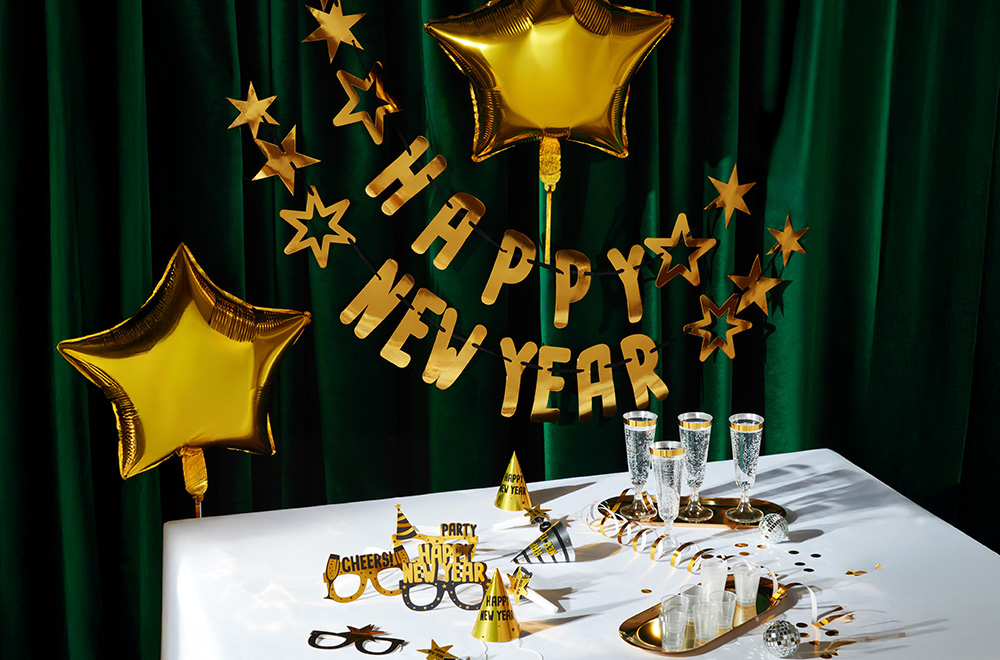Tisch für Silvester dekoriert, mit Ballons, Gläsern und goldenen Dekorationen.