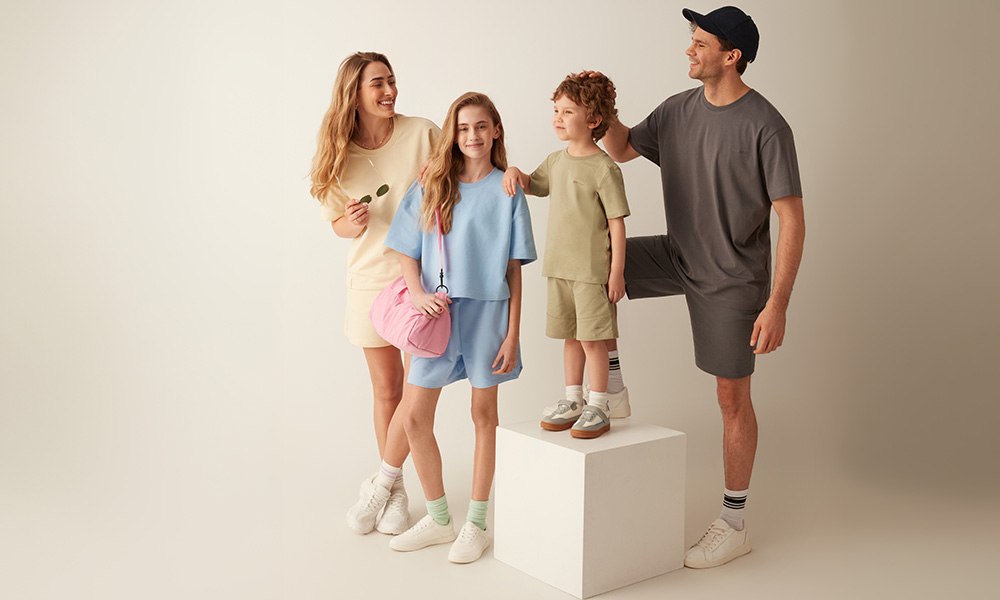 Eine Familie in pastellfarbener Kleidung posiert gemeinsam vor hellem Hintergrund.